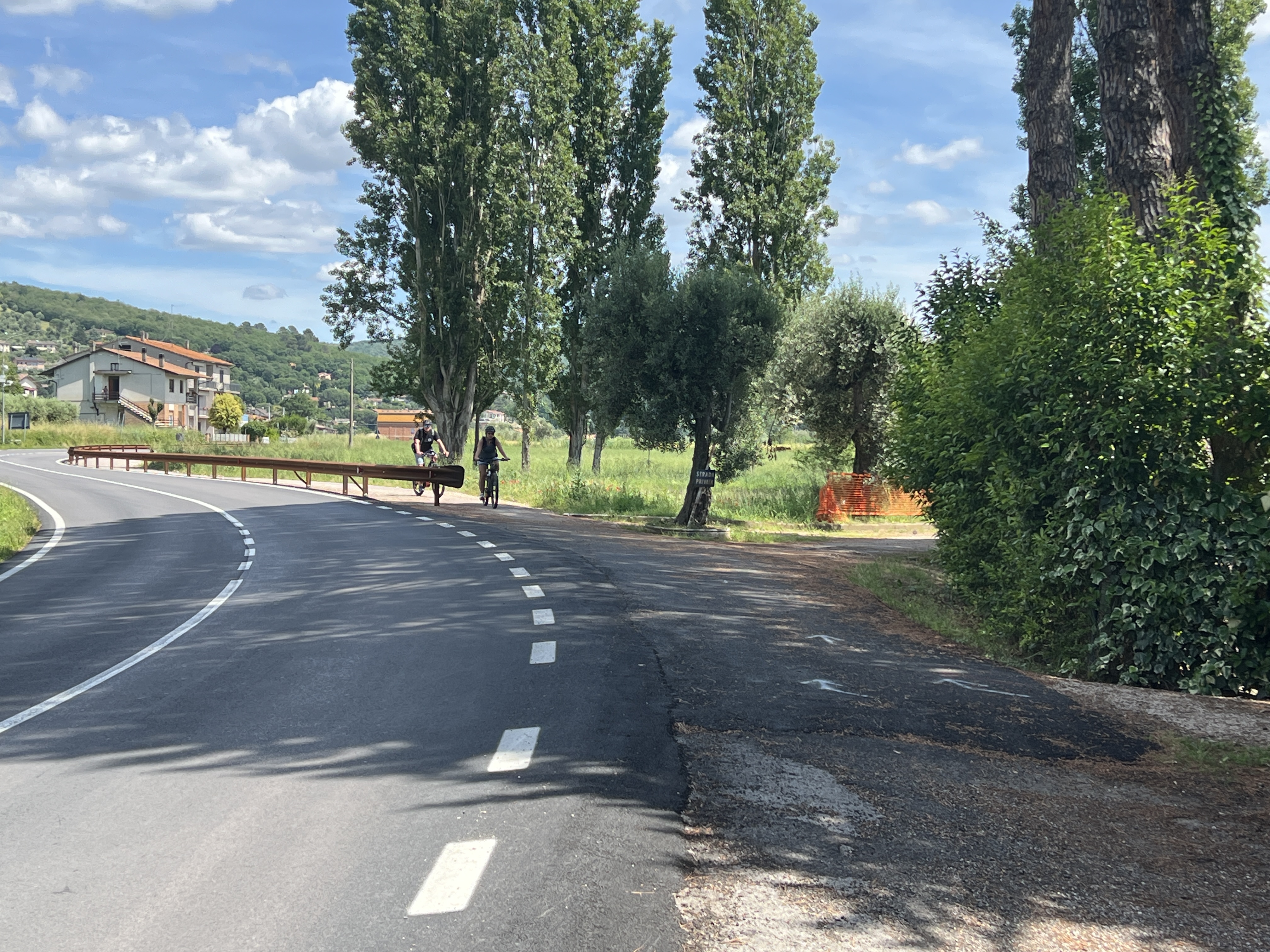 Trasimeno cycleway on the way out of San Feliciano. A paved road curves to the left. On the right is a bicycle path.